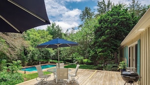 A wooden deck with a pool table, chairs, and a barbecue grill.