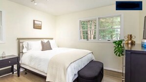 A bedroom with a bed, bedside table, bench, window, and a plant.