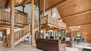 Een ruim interieur van een blokhut met een centrale trap, een gezellige zithoek met een bruine leren bank, en een eethoek met een tafel en stoelen.