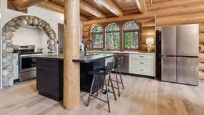 Een moderne keuken met een stenen boog, houten balkenplafond, een groot eiland met barstoelen en een roestvrijstalen koelkast.