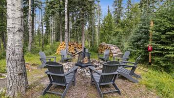 En skogsmiljö med en eldstad och fyra Adirondack-stolar placerade runt den.
