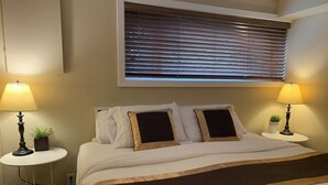 Et hotelværelse med en stor seng, to sengeborde med lamper, et vindue med persienner og en lille plante på et af bordene.