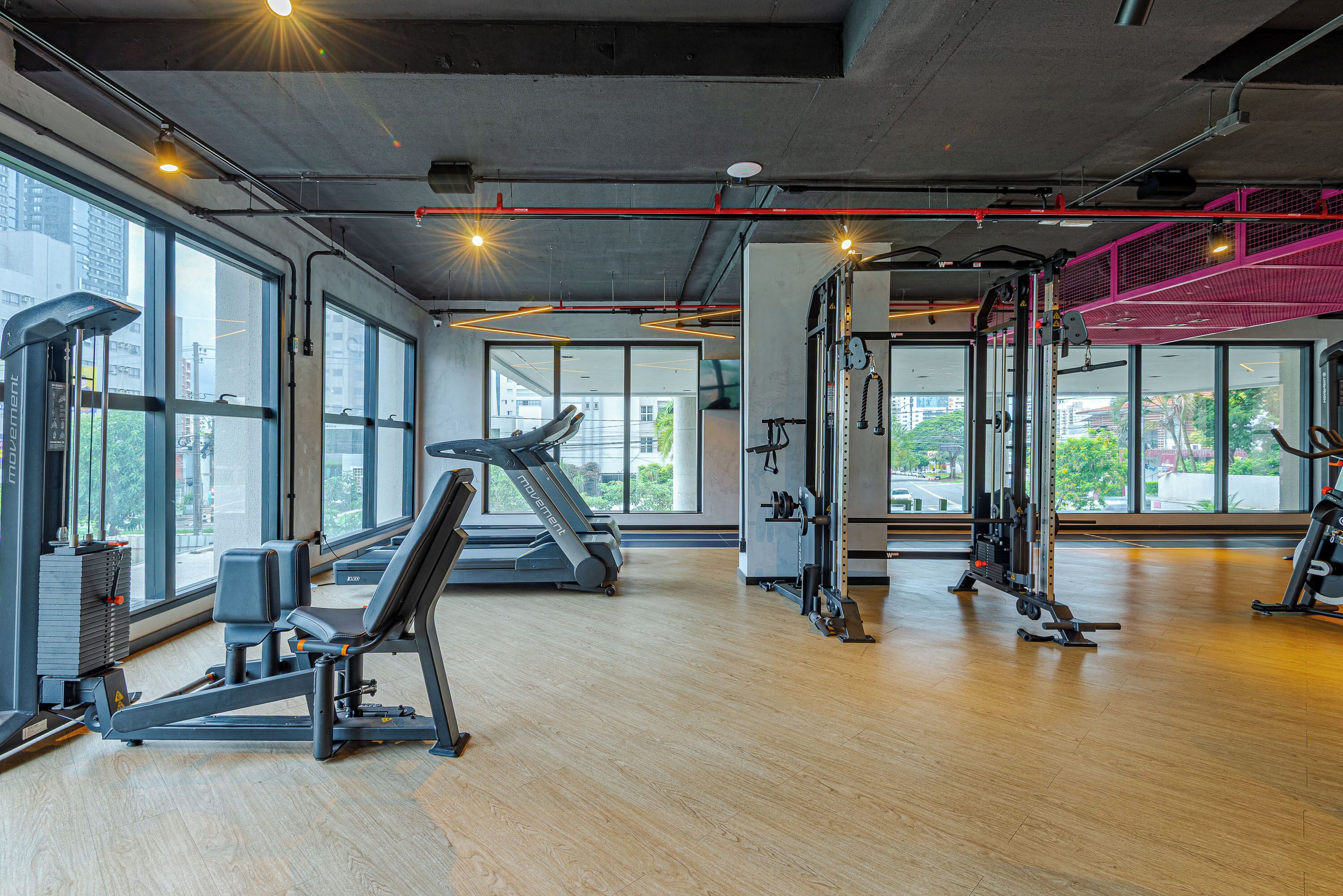 A gym with exercise equipment, large windows, and a concrete ceiling.