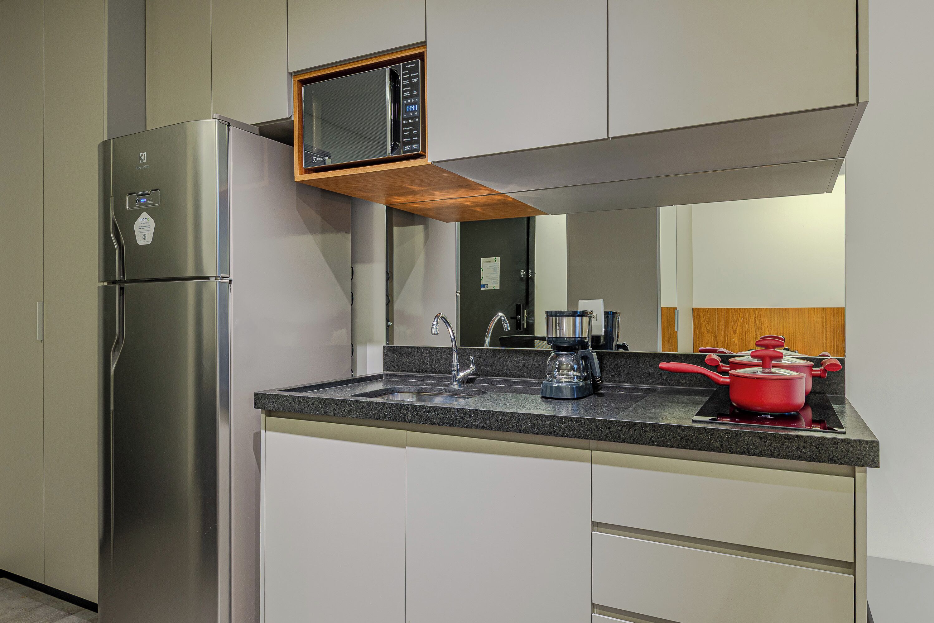 Una cucina con frigorifero in acciaio inox, forno a microonde, lavello e una pentola rossa sul fornello.