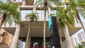 A tall hotel with a modern architectural design, featuring a prominent entrance with a glass facade and palm trees in the foreground. - Roomo Transamerica Goiânia Marista Urbà (Goiania)