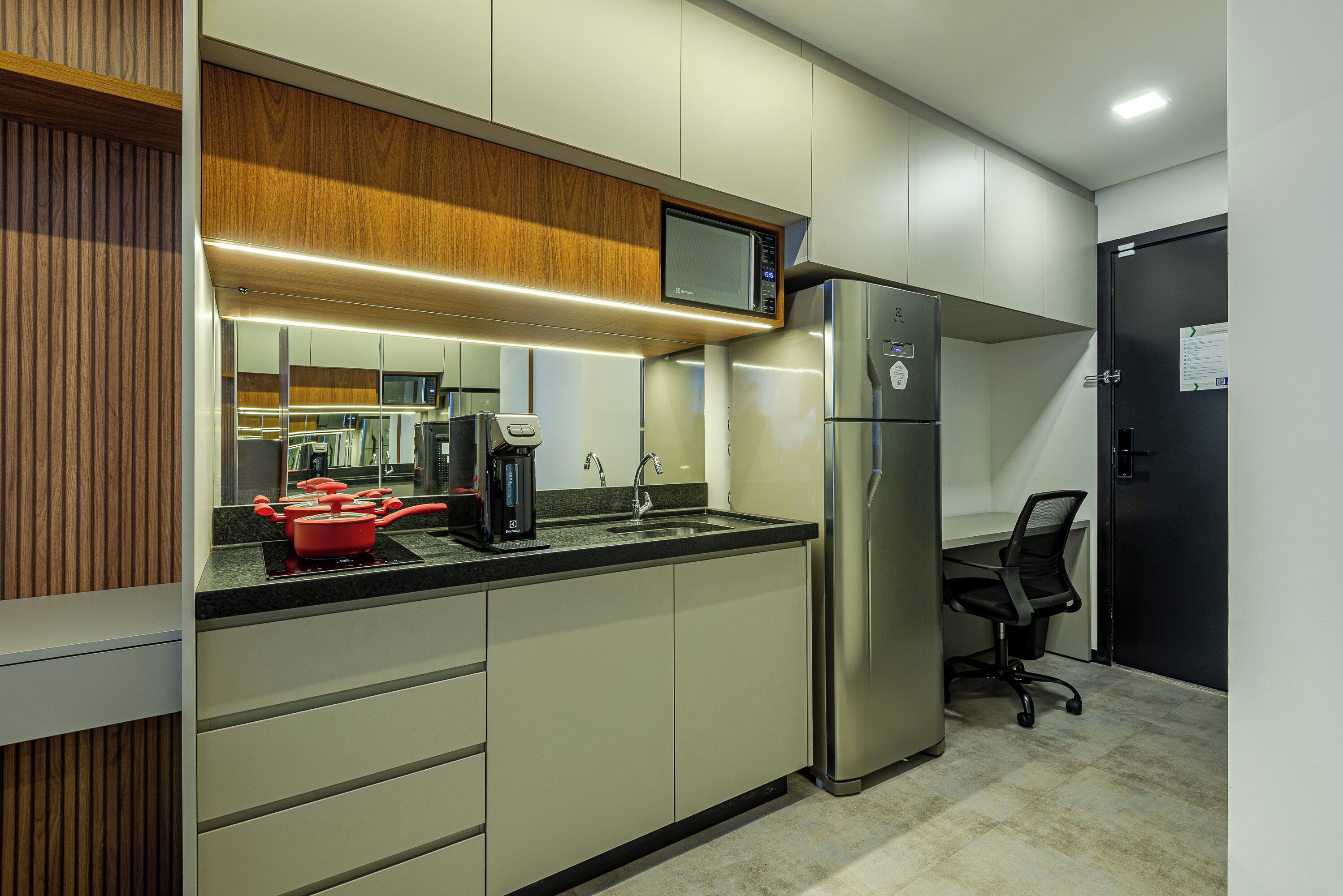 A modern kitchen with a microwave, refrigerator, and red pot on the counter.