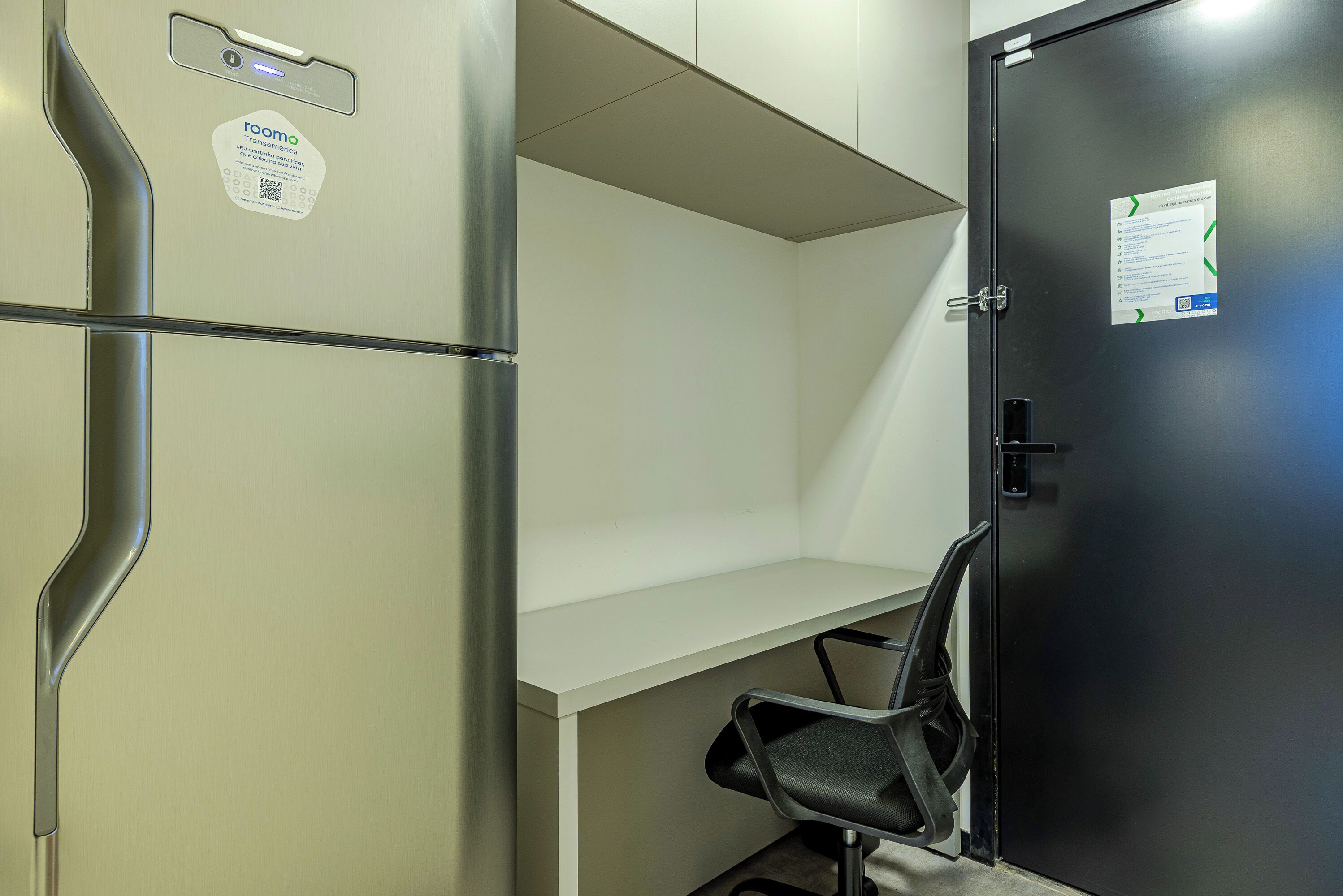 A room with a metal-framed door, a white desk, and a black office chair.