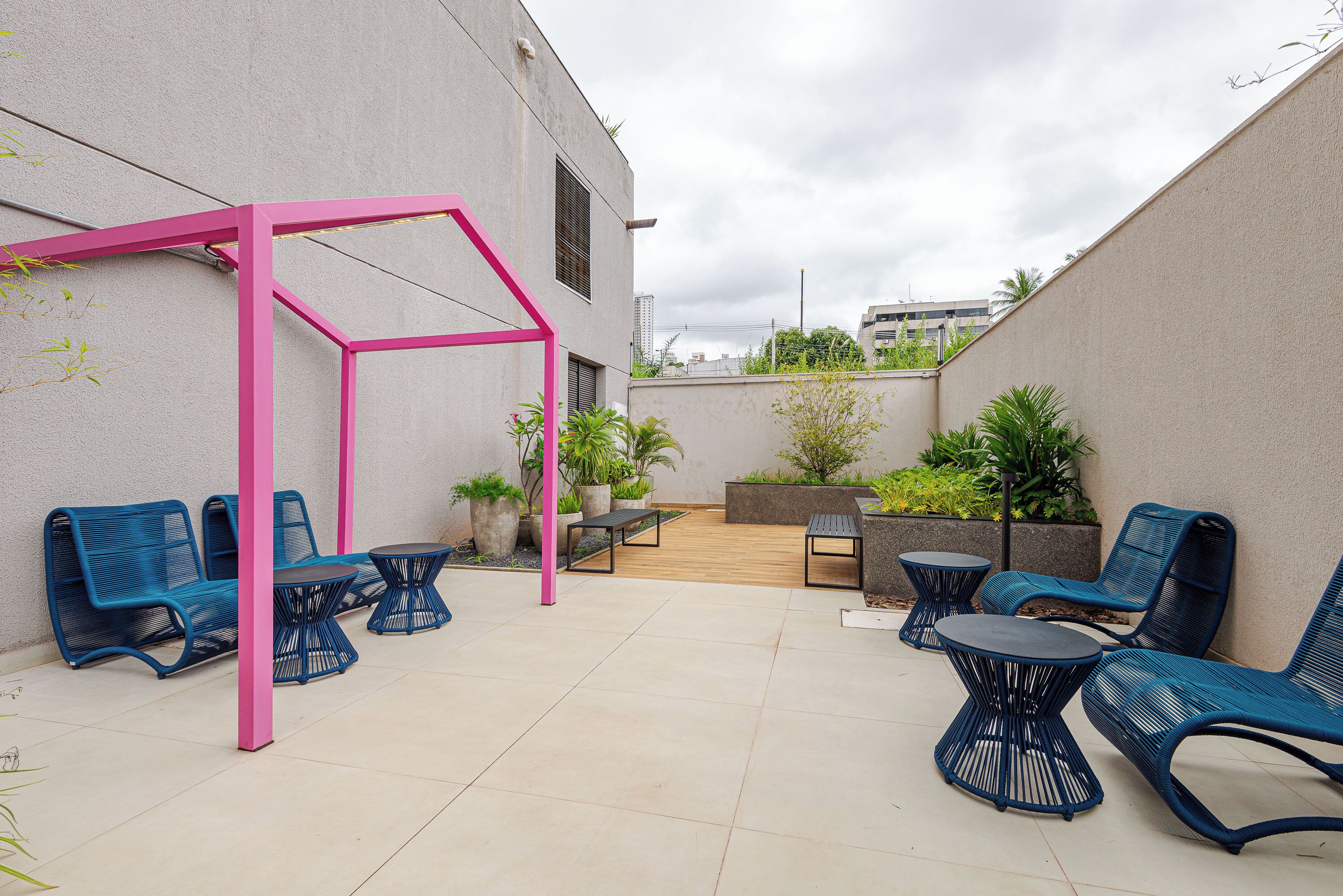 Un patio exterior con sillas azules, una pérgola rosa y una terraza de madera.