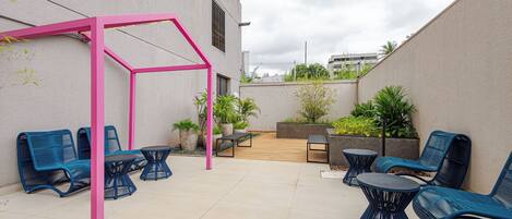 An outdoor patio area with blue chairs, a pink pergola, and a wooden deck.