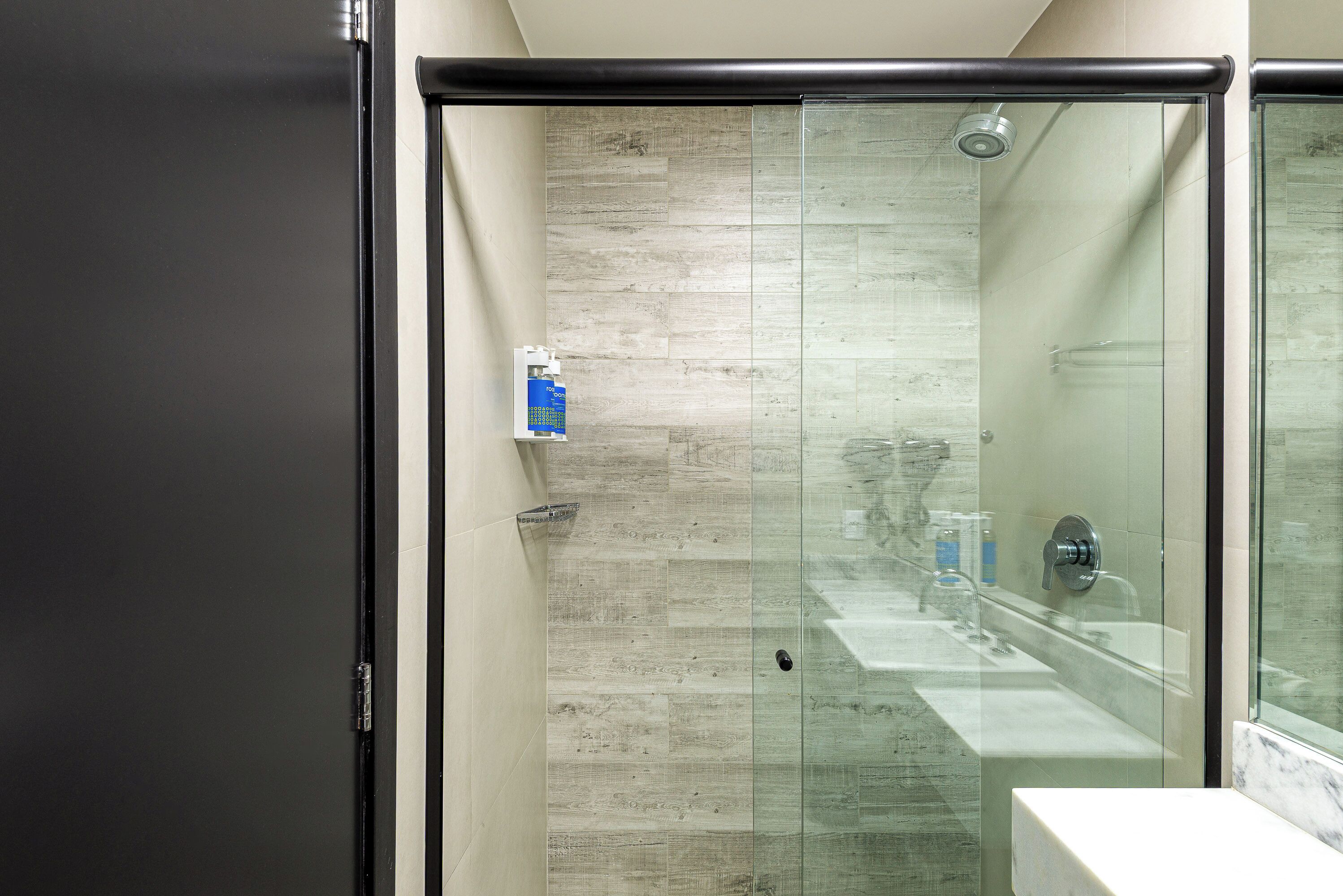A modern bathroom with a glass shower enclosure, a marble countertop, and a visible electrical outlet.