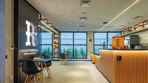 A modern cafe with a large window, a counter with a menu, and a seating area with chairs and a table. - Roomo Transamerica Goiânia Marista Urbà (Goiania)