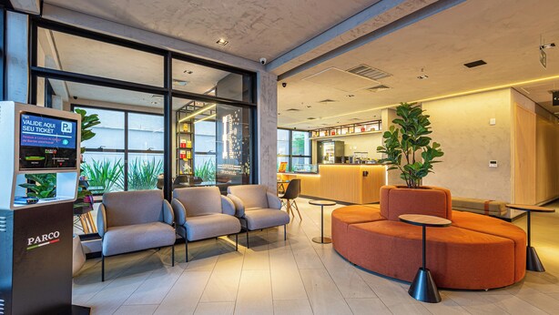 A modern hotel lobby with seating areas, a coffee bar, and a parking ticket machine. - Roomo Transamerica Goiânia Marista Urbà (Goiania)