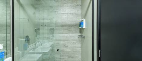 A modern bathroom with a glass-enclosed shower, a white sink, and a small shelf with toiletries.