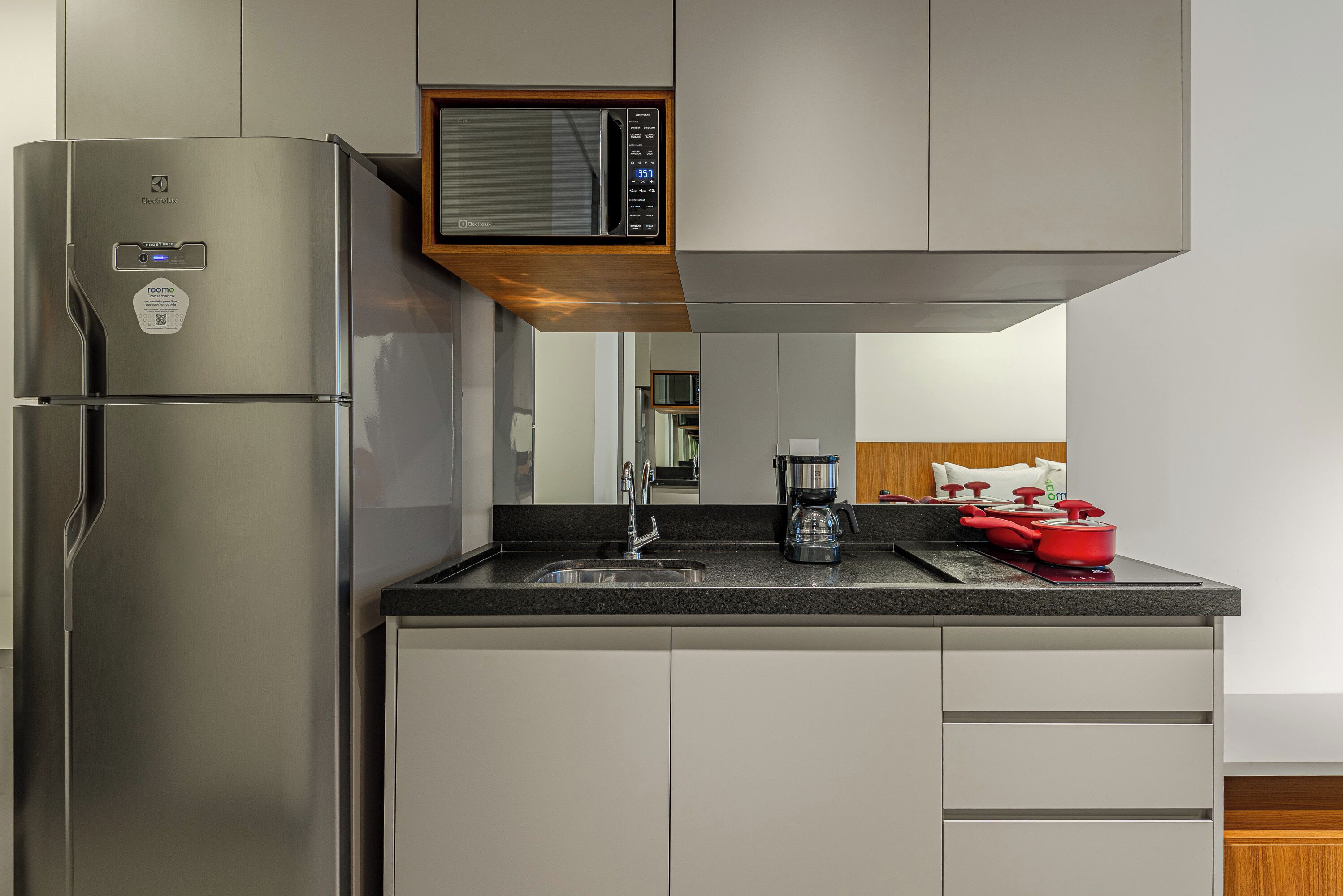 A modern kitchen with a built-in microwave, a coffee maker, and red cookware on the counter.