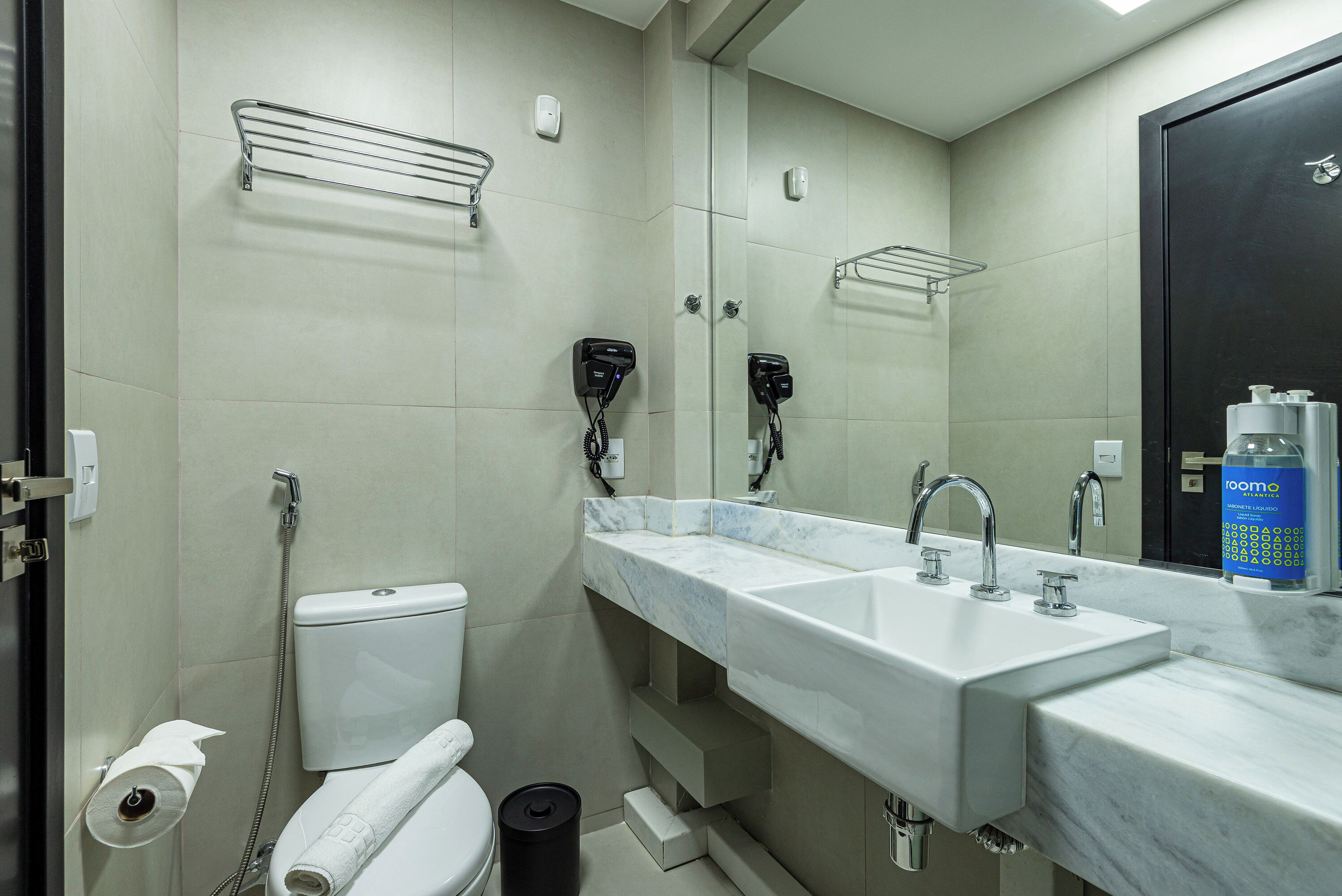 A modern bathroom with a white toilet, two sinks, a large mirror, and a shower area.
