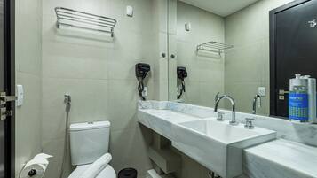 A modern bathroom with a white toilet, two sinks, a large mirror, and a shower area.
