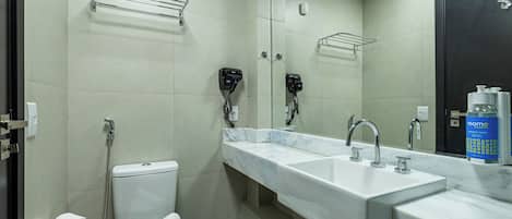 Uma casa de banho moderna com sanita branca, duas lavatórios, um espelho grande e zona de duche.