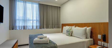 A hotel room with a bed, bedside table, and a window with curtains.