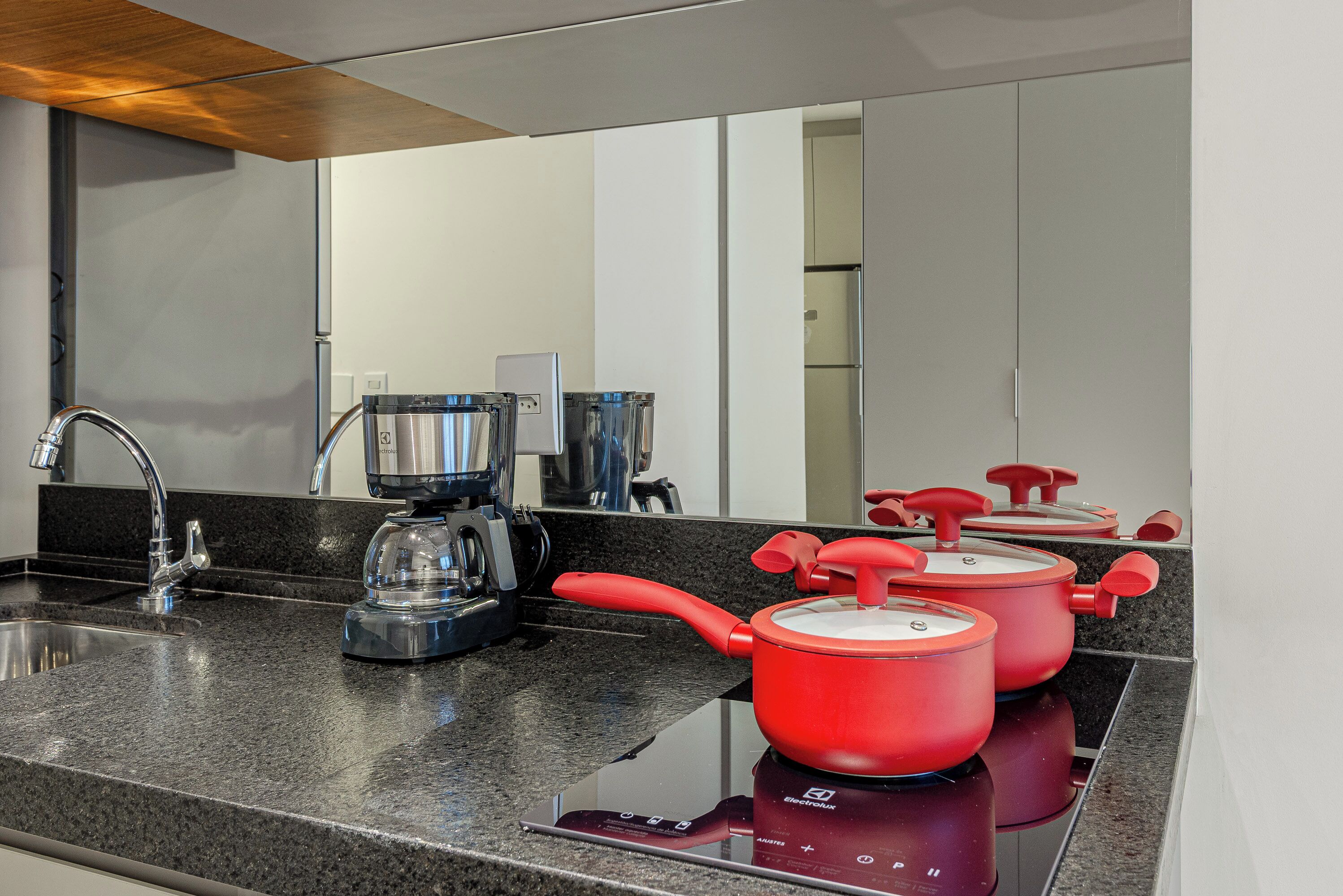 A modern kitchen with granite countertops, a stainless steel sink, a coffee maker, and red pots on an induction cooktop.
