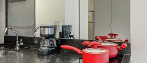 A modern kitchen with granite countertops, a stainless steel sink, a coffee maker, and red pots on an induction cooktop.