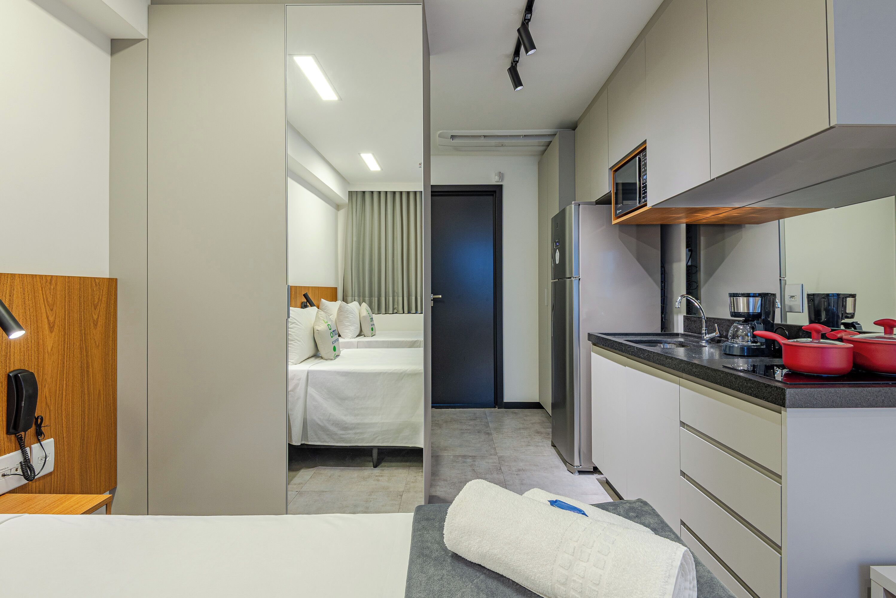 Una habitación de hotel con cama, escritorio, teléfono, microondas y kitchenette.