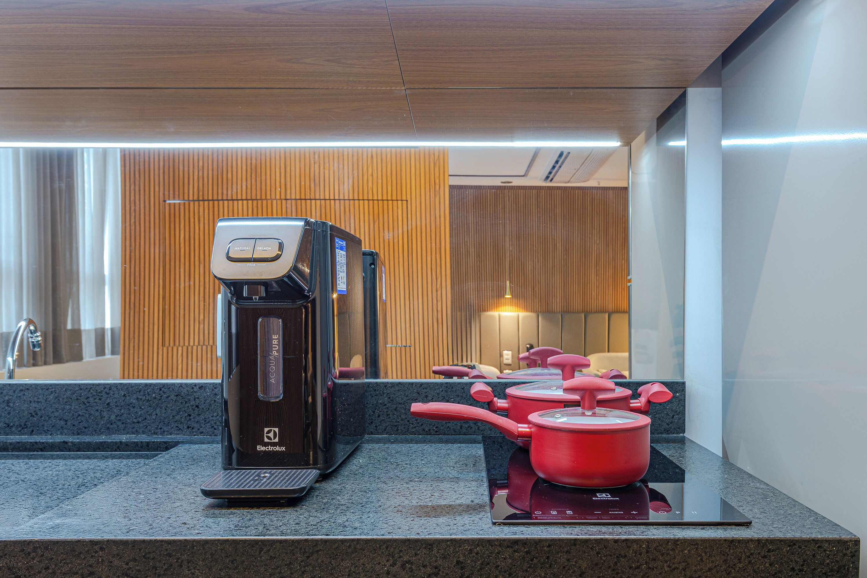 A modern kitchen with a coffee maker, a kettle, and red pots on an induction cooktop.