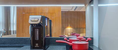 A modern kitchen with a coffee maker, a kettle, and red pots on an induction cooktop.