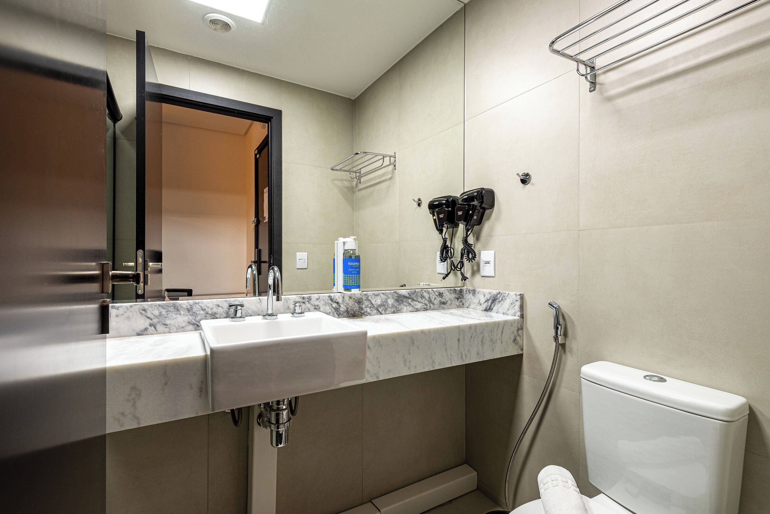 Un baño con lavamanos de mármol, inodoro y secador de pelo montado en la pared.
