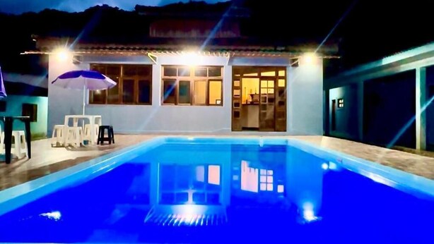 Une piscine avec un espace patio, un coin salon extérieur couvert et un bâtiment doté de grandes fenêtres.