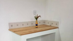 Une pièce d’angle avec un bureau blanc, un vase contenant des plantes séchées et un sol recouvert de carreaux verts.