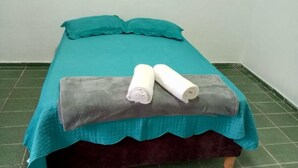 Un lit avec une couette et des draps de couleur turquoise, deux serviettes blanches roulées et une couverture grise.
