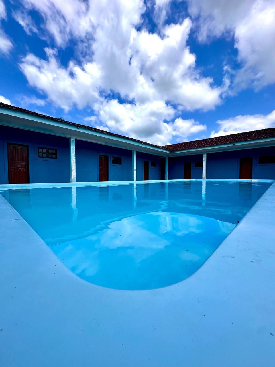 A swimming pool with a blue-tiled floor, surrounded by buildings with blue walls and red-tiled roofs.