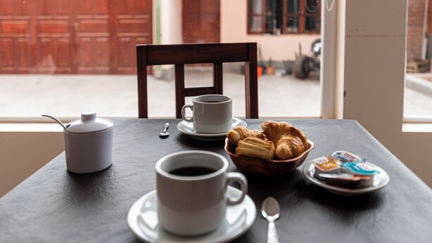 A table with a cup of coffee, a bowl of croissants, and a plate of yogurt. - Ñañitas Tampu Wasi (Maimara)