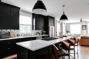 Een moderne keuken met zwarte kasten, een wit aanrechtblad en een centraal eiland met barstoelen. Er is een zithoek met een bank en een salontafel.