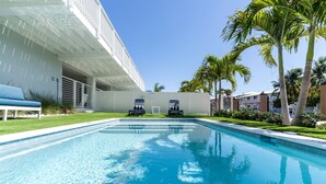 A swimming pool with lounge chairs, palm trees, and a modern building with a white facade.