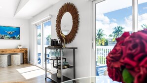 A modern living room with a large oval mirror, a wooden coffee table, and a view of palm trees through large windows.