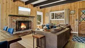 Una sala de estar acogedora con chimenea de ladrillo, paredes de madera, un ventanal grande y un rincón de estar confortable.