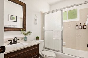 Un bagno moderno con lavabo in marmo, mobile contenitore in legno scuro, box doccia in vetro e water bianco.