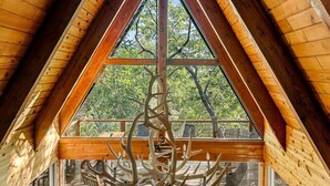 Acogedor dormitorio en ático con techo inclinado de madera, un ventanal grande y un sofá de cuero con almohadones decorativos.