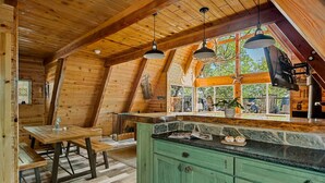 Una cabaña de madera acogedora con comedor, encimera de piedra y un amplio ventanal con vistas al exterior.