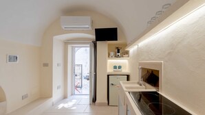 A narrow hallway leading to a door, a small refrigerator, a microwave, and a built-in stove. - Laggetto Corner (Otranto)