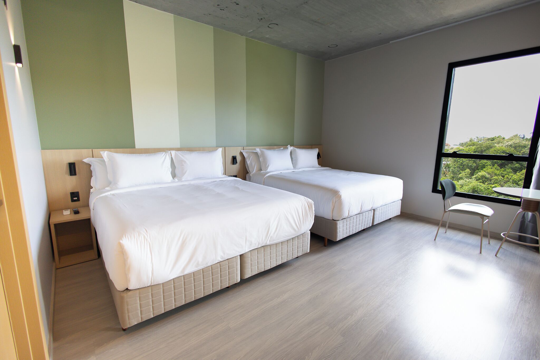 Quarto de hotel com duas camas, uma mesinha e uma janela com vista.