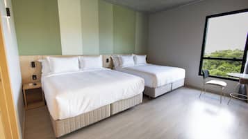 Quarto de hotel com duas camas, uma mesinha e uma janela com vista.