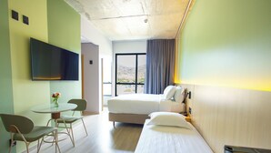 Habitación de hotel con cama, escritorio con silla, televisor montado en la pared y ventana con cortinas.