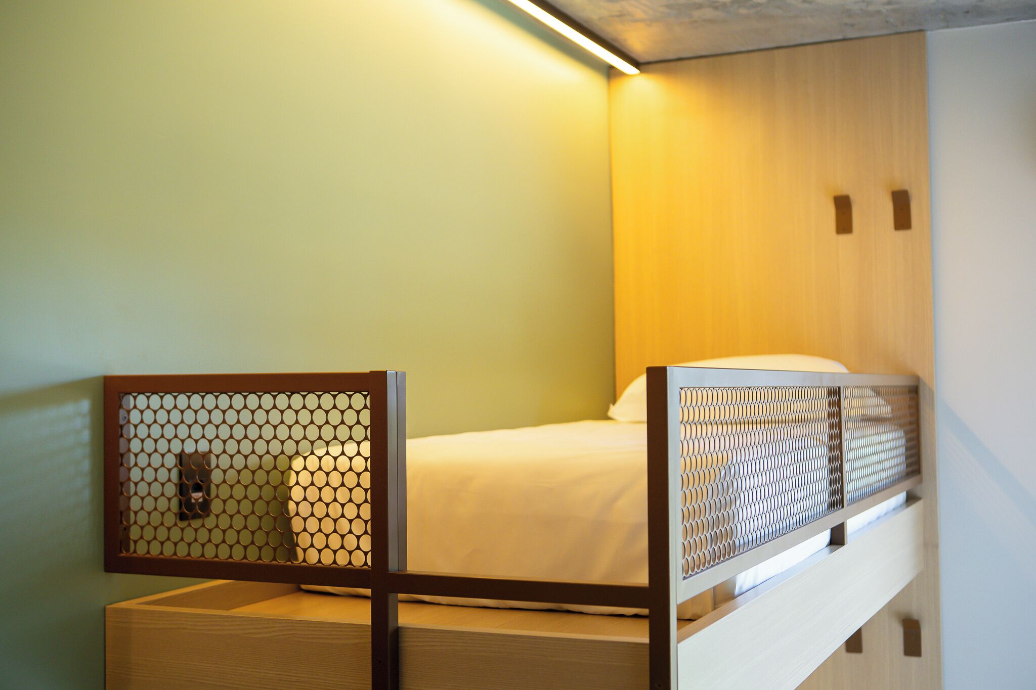 A bunk bed with a wooden frame and a mesh headboard, a white mattress, and a wooden headboard.