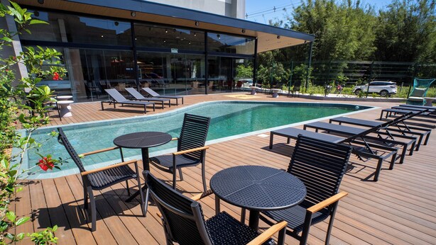 Zona junto a la piscina con sillones, mesas y un edificio moderno con ventanales de vidrio.