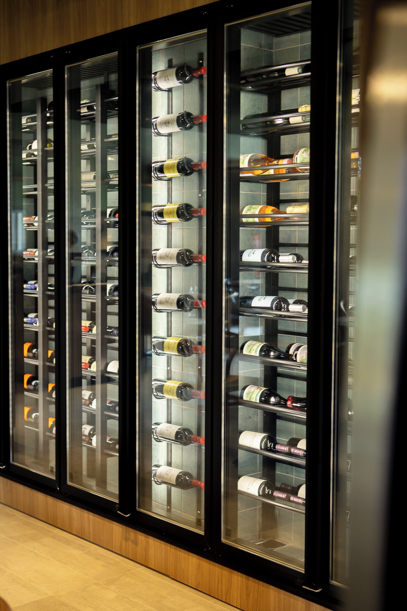 A wine cellar with multiple glass-fronted shelves holding various bottles.