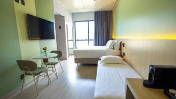 Habitación de hotel con cama, escritorio con cafetera, televisor montado en la pared y ventana con cortinas.