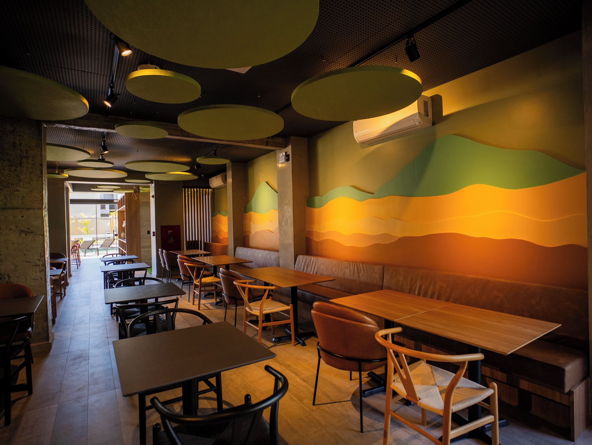 A restaurant interior with wooden tables and chairs, a long counter, and a mural on the wall.