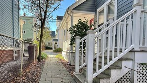 A residential pathway leading to a house with a white staircase and a picket fence.